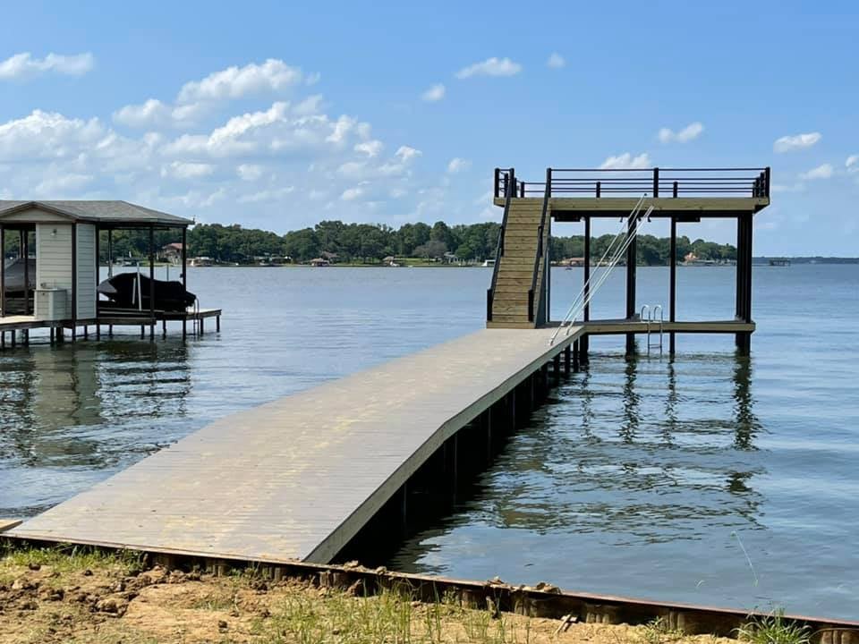 View further away of a deck on the water with stairs leading to a top level deck and stairs down into the water