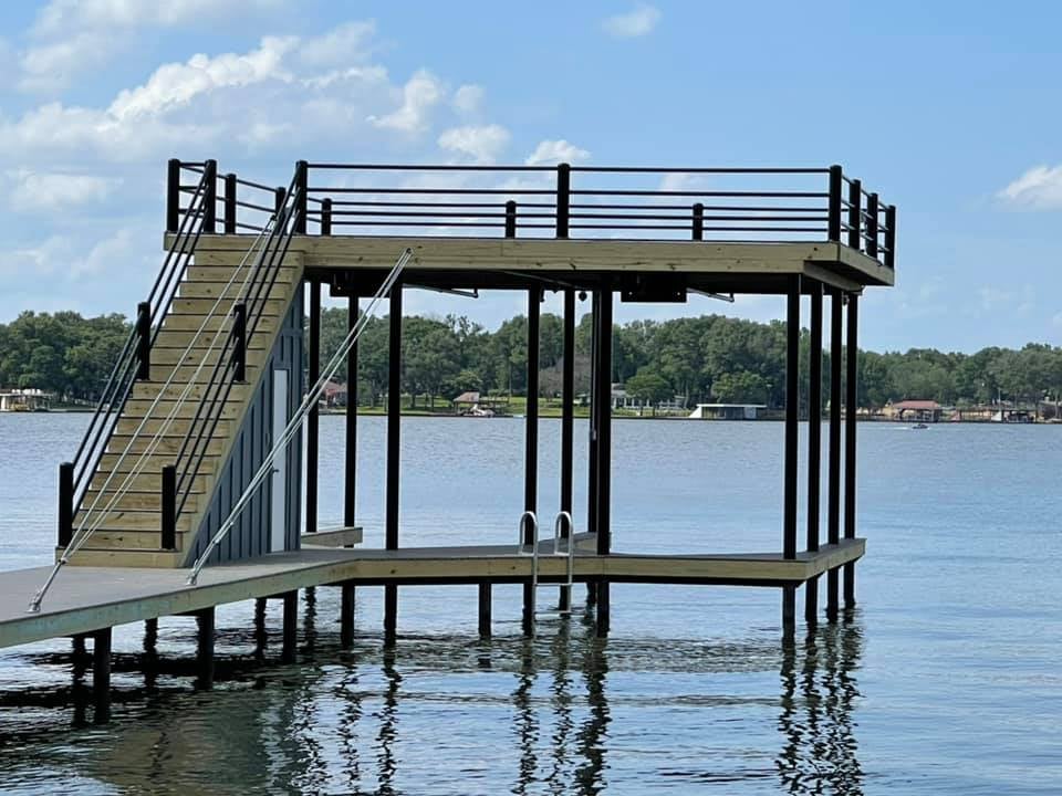 Side angle of a deck pictured on the water with stairs leading to a top level deck, and down into the water